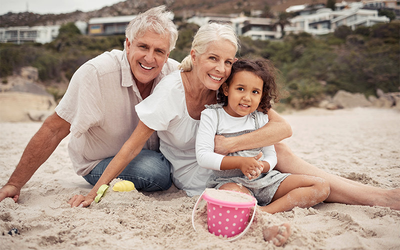 grandparents at the beach in the sand with their granddaughter